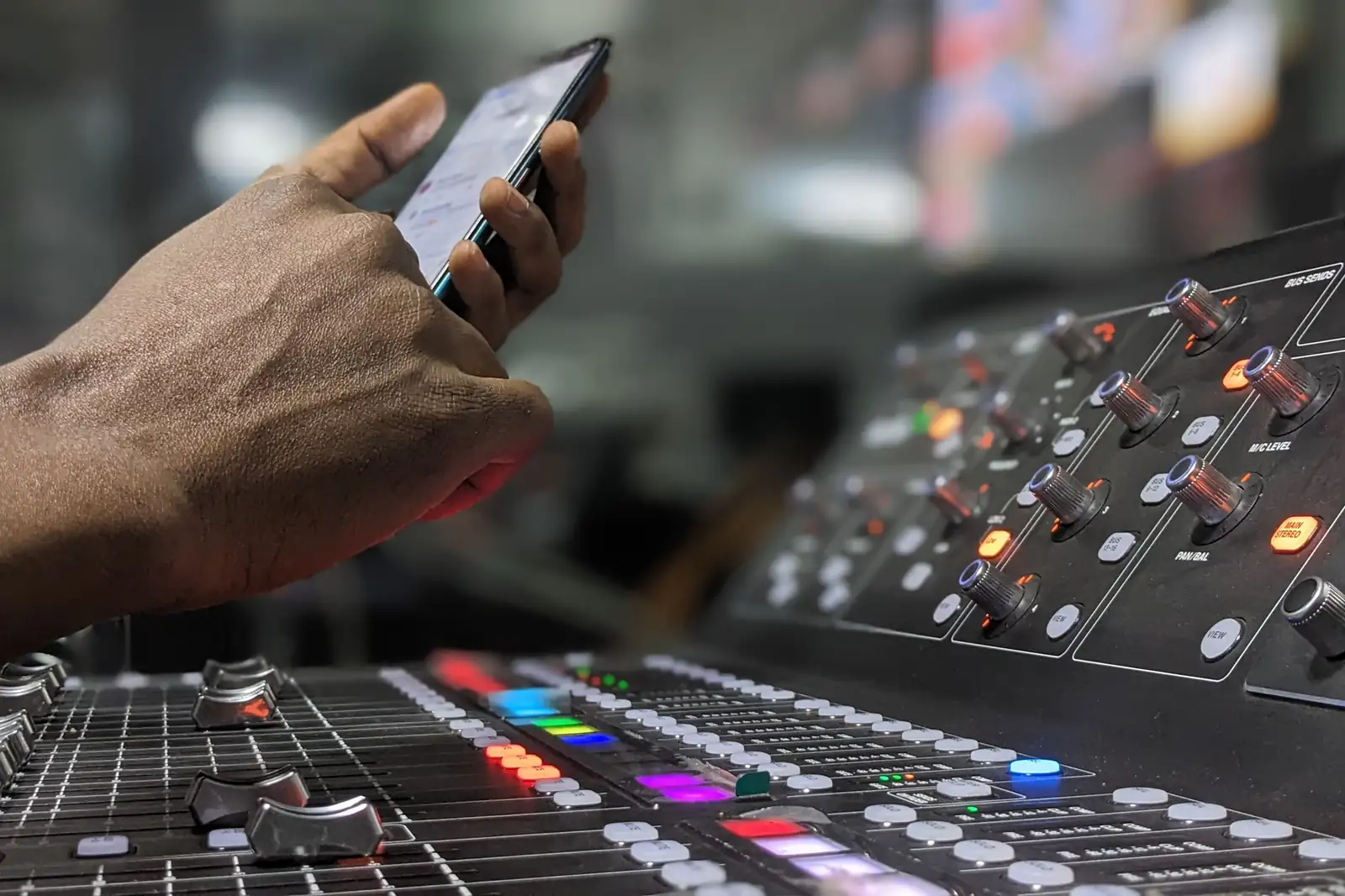 Hand holding a smartphone above the faders of a mixing console