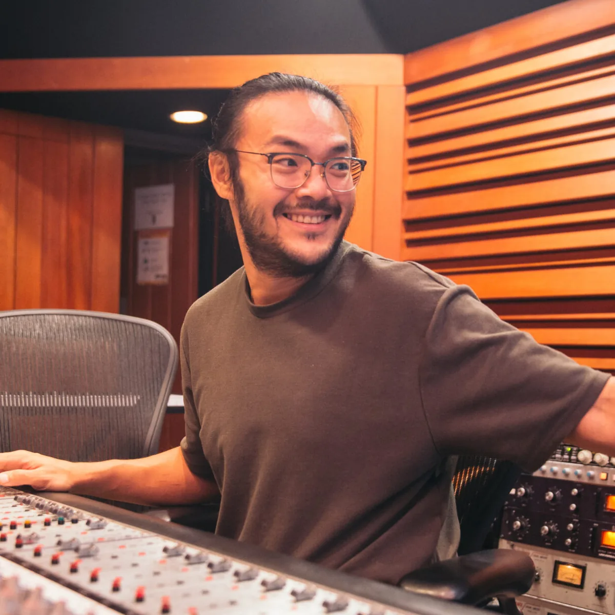 Alvin Wee smiling behind a large mixing console in a wood-panelled studio