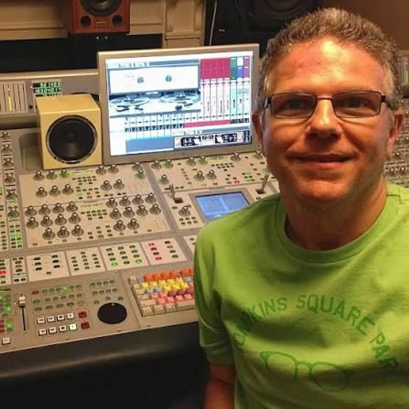 Michael Costa smiling at his mixing console, with a monitor and a speaker behind him
