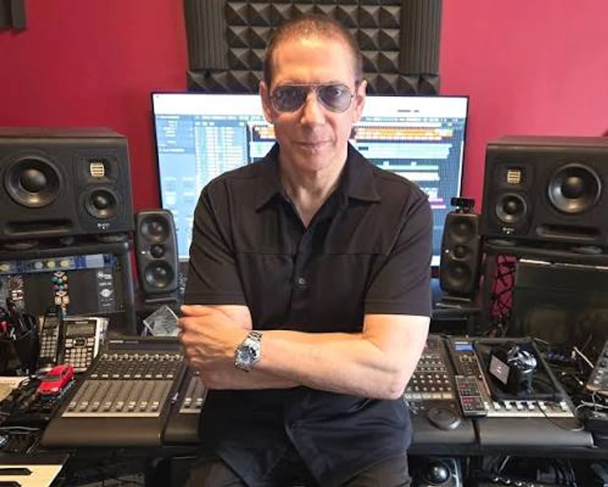 Scott Yahney with his arms folded in his studio, between monitor speakers and a control surface